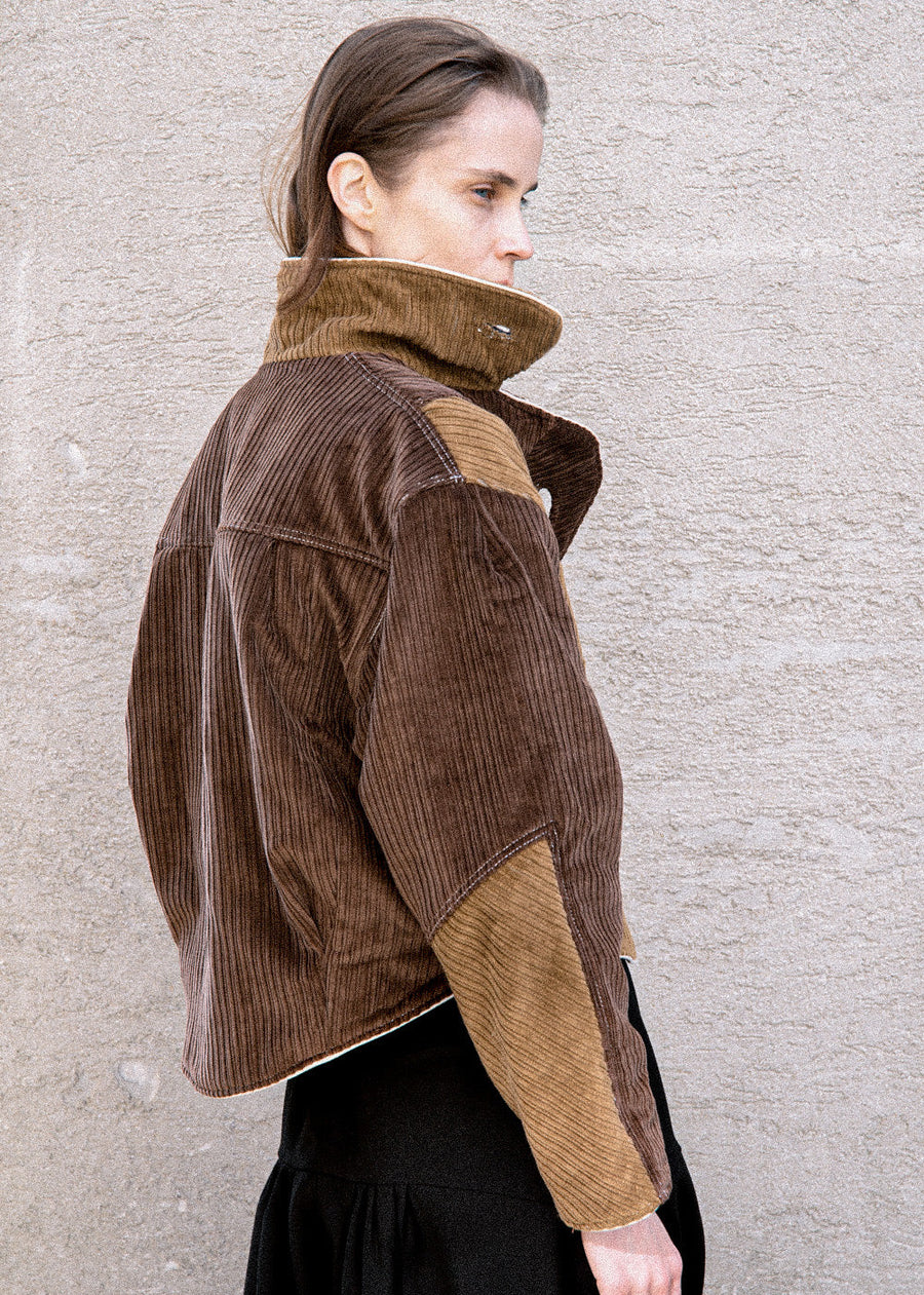 Woman wearing a brown corduroy jacket with a textured wall background
