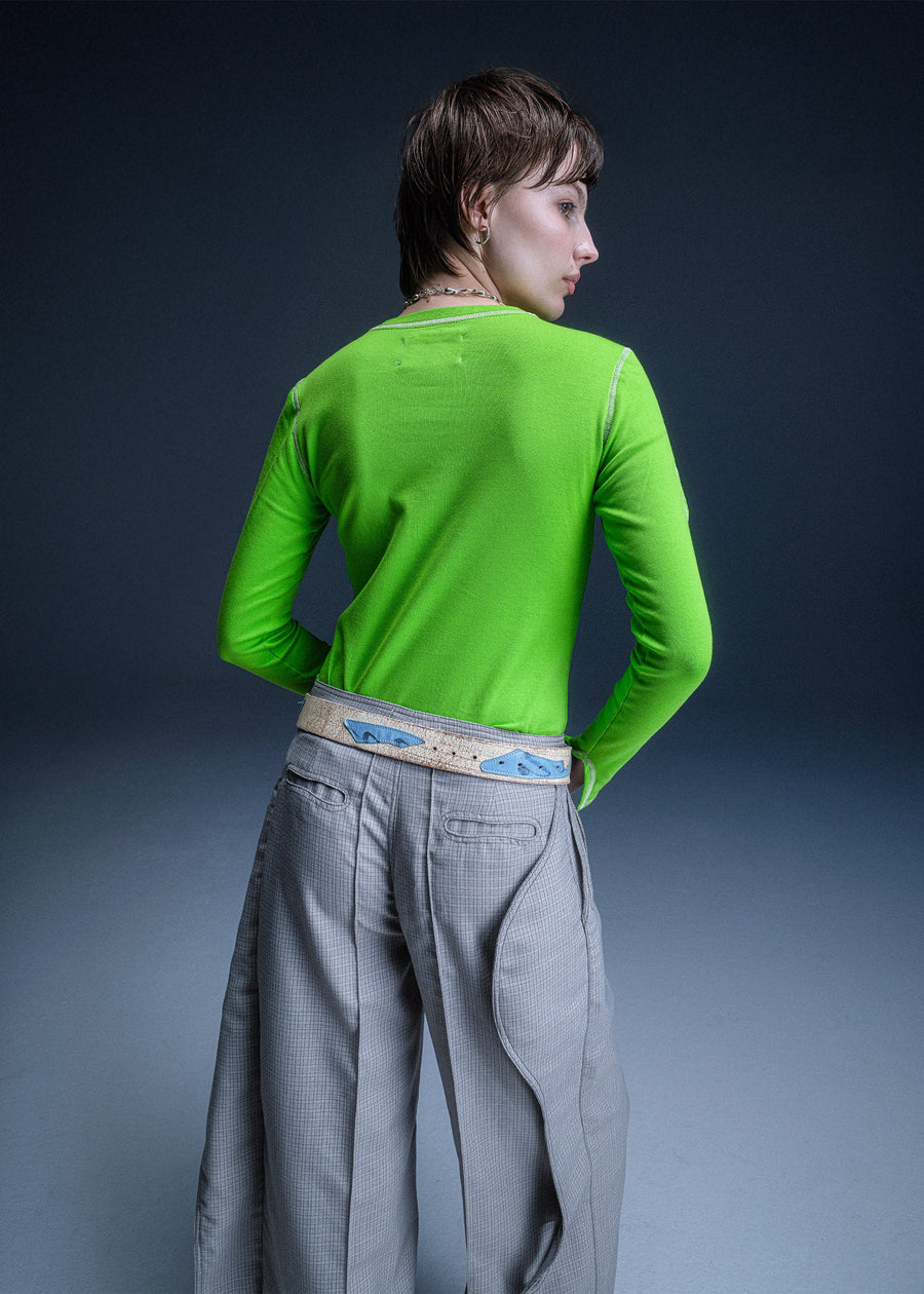 Person wearing a bright green long-sleeve top and gray pants against a dark background