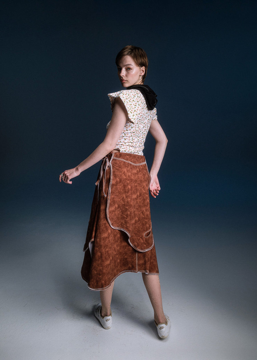 Woman wearing a white top with ruffled sleeves and a brown skirt on a dark background