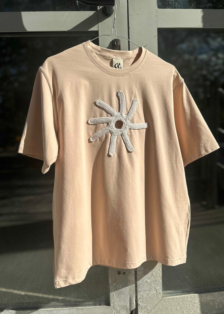 Beige t-shirt with a star-shaped design on a hanger.
